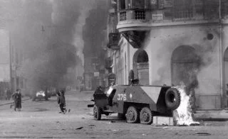 Een opname van de straatgevechten in Boedapest. Op de voorgrond een stukgeschoten Sovjet-pantserwagen.
