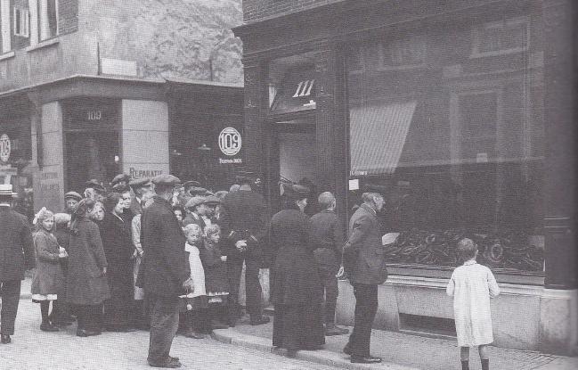 Klanten staan voor een slagerij in de Kleine Houtstraat in Haarlem in mei 1918 in de rij voor eenheidworst.