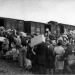 Mensen staan bepakt en bezakt te wachten bij de goederenwagons van een trein in doorvoerkamp Westerbork, 1942-1945