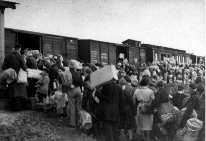 Mensen staan bepakt en bezakt te wachten bij de goederenwagons van een trein in doorvoerkamp Westerbork, 1942-1945