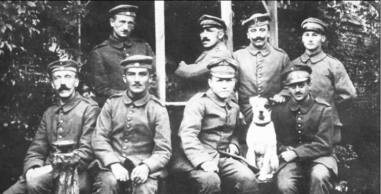  Hitler met zijn kameraden en zijn trouwe hondje Foxl in het gebied achter het front. Voorste rij van links naar rechts: Adolf Hitler, Balthasar Brandmayer, Anton Bachmann en Max Mund. Achterste rij van links naar rechts: Ernst Schmidt, Johann Sperl, Jakob Weiss en Karl Tiefenböck.