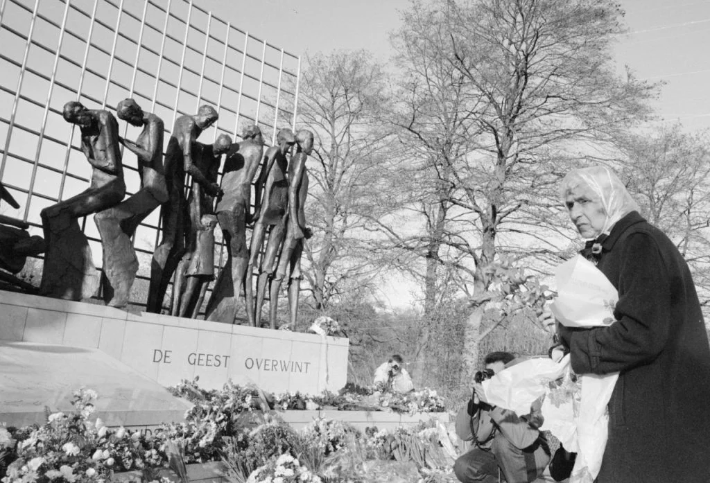 Vrouw met bloemen in de hand staat voor het monument. Stille bloemlegging voor slachtoffers uit de Tweede Wereldoorlog bij het Indisch Monument in Den Haag naar aanleiding van het overlijden van Keizer Hirohito van Japan. (cc - Erfgoed in Beeld)