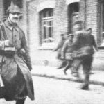 Bataljonskoerier Adolf Hitler in mei 1915 met zijn geweer over zijn schouder gehangen. Hitler is onderweg om een boodschap af te leveren. Deze foto verschijnt voor het eerst in de regimentsgeschiedenis van het 16e RIR.