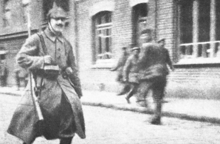 Bataljonskoerier Adolf Hitler in mei 1915 met zijn geweer over zijn schouder gehangen. Hitler is onderweg om een boodschap af te leveren. Deze foto verschijnt voor het eerst in de regimentsgeschiedenis van het 16e RIR.