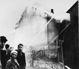 Terwijl de synagoge in Ober-Ramstadt op de ochtend na de Kristallnacht in de brand staat, kijken omwonenden toe. Brandweermensen voorkomen dat het vuur overslaat naar naburige panden. (Bron: U.S. Holocaust Memorial Museum)