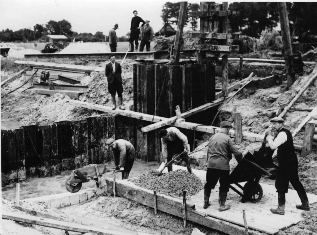 Aanbrengen van de onderbouw van een stuw in de Wold Aa. Veel werk wordt gedaan met mankracht. De foto is genomen (in het kader van de A2 werken) voor het waterschap de Wold Aa. Ten behoeve van verbetering van het stroomgebied van de Wold Aa. (Drents Archief)