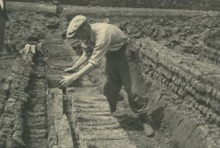 Een onbekende man bezig met het verstapelen van drogende fabrieksturf (laatste stadium) ten behoeve van ruilverkaveling Zegveld, provincie Utrecht. Deze foto is genomen in de gemeente Schoonebeek (Drents Archief)