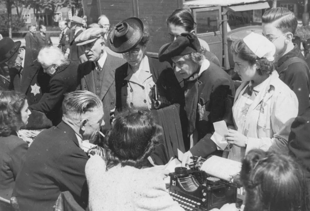 Medewerkers van de kampadministratie van kamp Westerbork schrijven op het Olympiaplein in Amsterdam (op de sportvelden) honderden joden in op 20 juni 1943, die daarna naar kamp Westerbork worden overgebracht. Foto: gemaakt door Herman Heukels (publiek domein). Beeldbank WO2, collectie NIOD.