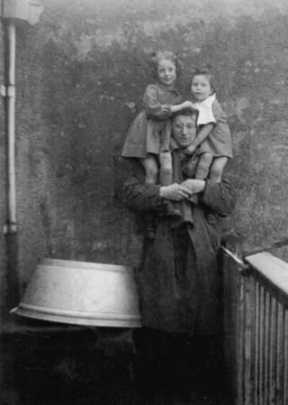 1952. Zus Marjolein en Catherine op de schouders van hun vader, op het balkon. Het gezin woonde toen op de Zuidwal in Den Haag.