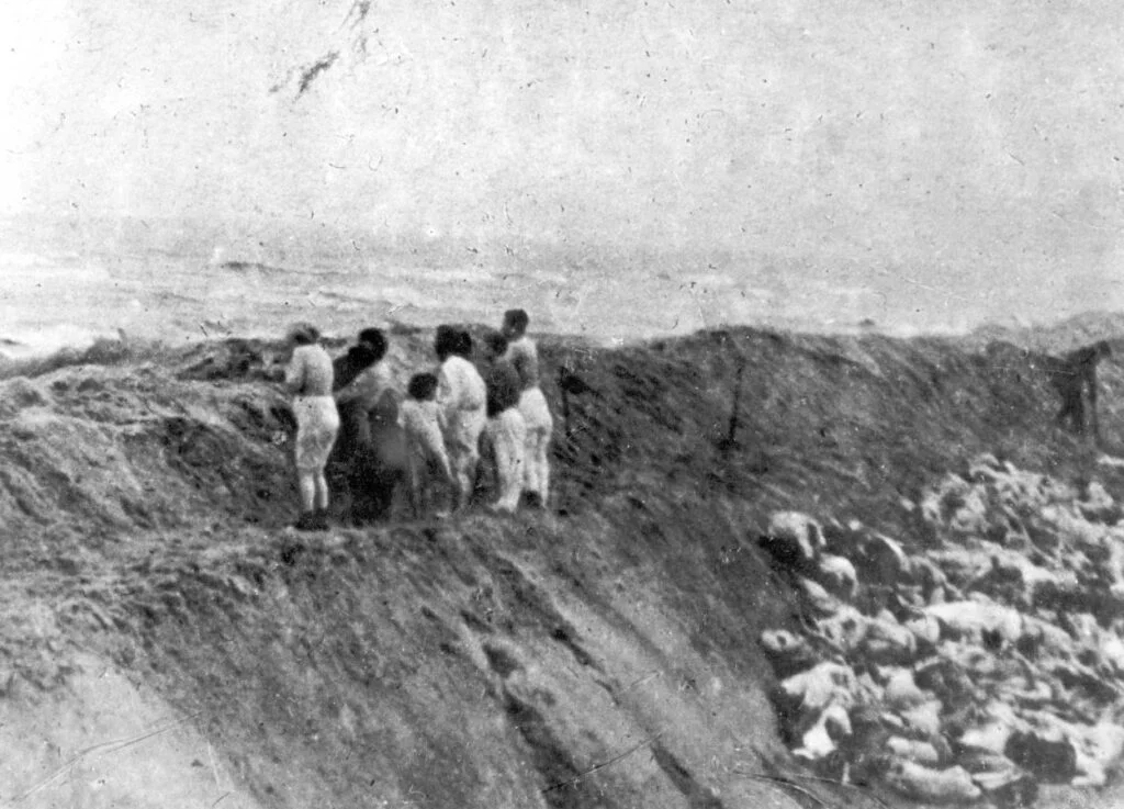 ‘Joodse vrouwen en kinderen uit Liepāja staan op de rand van een put vooraleer vermoord te worden, 15 december 1941 – foto gemaakt door Oberscharführer Carl-Emil Strott (Yad Vashem Photo Archive, Jerusalem, archival signature 1979/5).