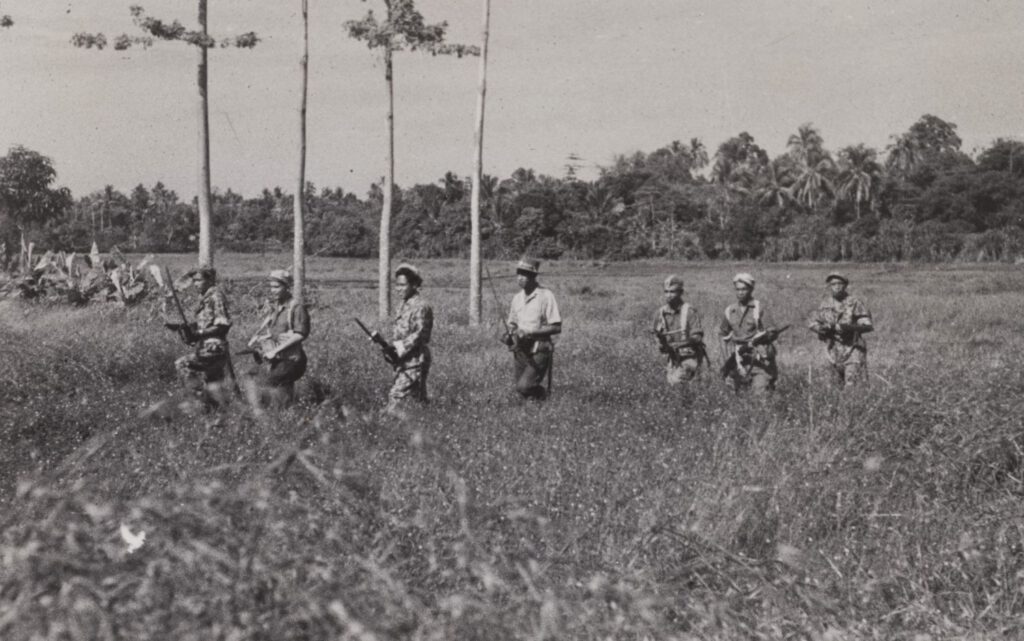 Een KNIL-patrouille in de eerste fase van de dekolonisatie-oorlog in Indonesië. De manschappen lopen dicht bij elkaar, een les uit onder meer de Atjeh-oorlog die echter vanaf 1945 onnodig slachtoffers bleek te eisen aangezien de Indonesiërs over vuurwapens beschikten. Twee van de mannen hebben ook een klewang in de hand. 