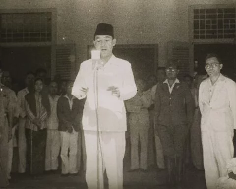 Soekarno leest de Indonesische onafhankelijkheidsverklaring voor. Rechts in witte kleding Hatta. Het is 17 augustus 1945 en heel veel is nog onzeker.