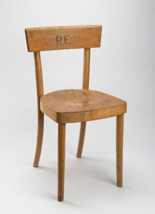 Houten stoel voorzien van brandmerk RE (Rijks Eigendom) bestemd voor de inrichting van de Molukse woonbarakken. Collectie privé-eigendom bruikleengever.