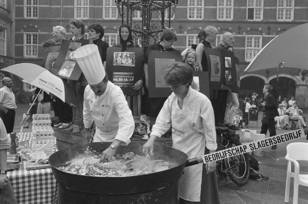 Barbecue op Binnenhof (1988). Slagers braden vlees, onder toeziend oog van enkele leden van de actiegroep Lekker Dier