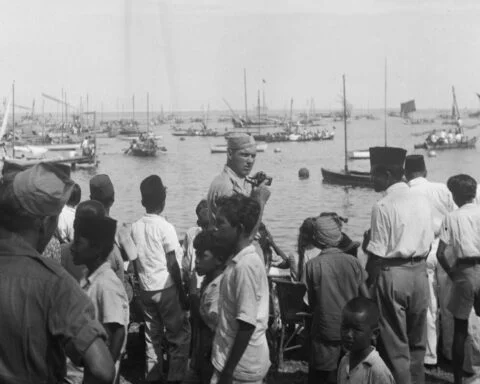 Nederlandse militair met camera tijdens een roeiwedstrijden met prauwen ter gelegenheid van Koninginnedag - Makassar, 1948