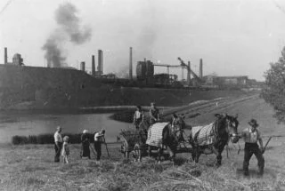 Boeren hooien in de schaduw van de staalfabriek van Völklingen omstreeks 1947. Het Saarland, een Frans-Duitse grensregio en oud industriegebied, was sinds het in de jaren 1850 werd geïndustrialiseerd lang een bastion van mijnbouw en metallurgie.