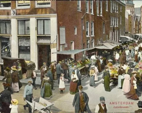 Prentbriefkaart uit 1908 met een ingekleurde foto van de Jodenbreestraat, hoek Uilenburgersteeg. Collectie Joods Museum.