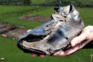 Een van de gevonden schoenen, met op de achtergrond de opgravingslocatie